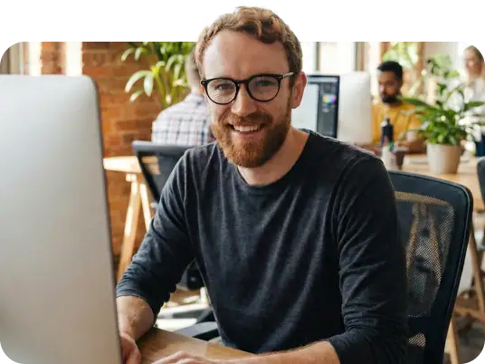 Friendly man with glasses works on a computer in a modern office.