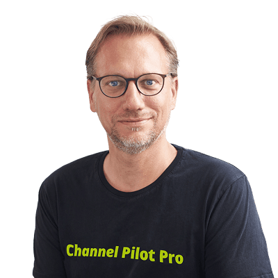 Mann trägt T-Shirt mit "Channel Pilot Pro" Aufdruck, lächelnd, vor grünem Hintergrund.