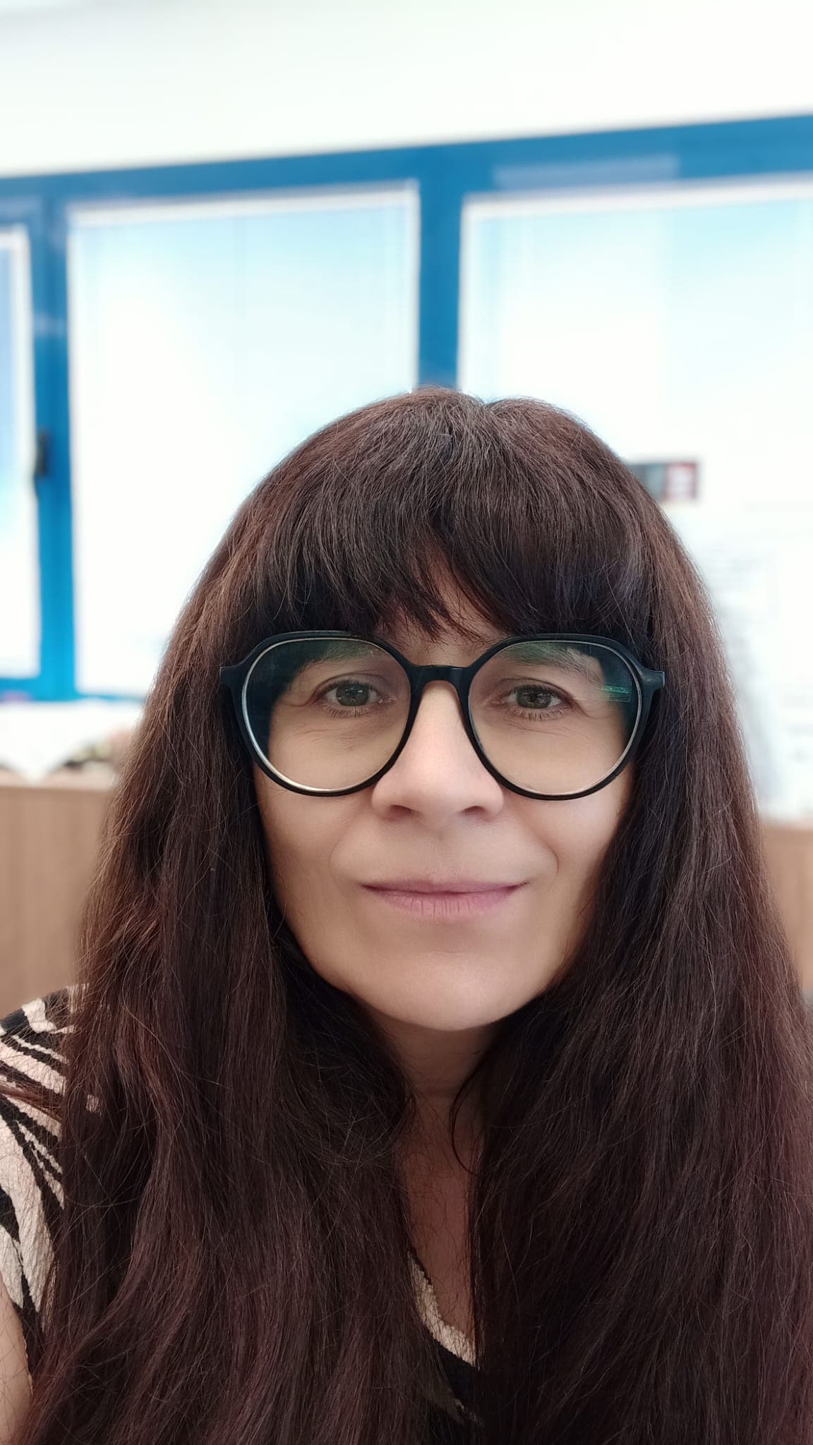 Woman with glasses in front of an office window, smiling.