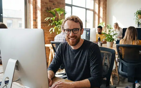 Mann arbeitet glücklich an Computer im Büro.