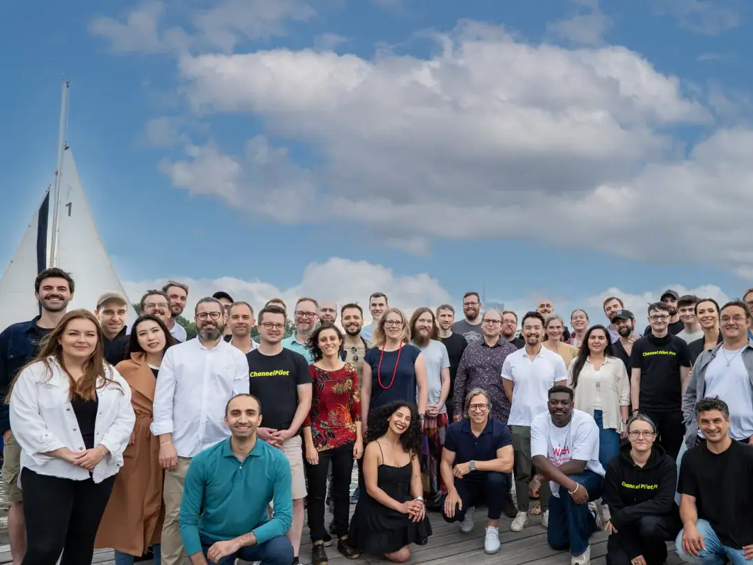 Großgruppe von Menschen am Wasser mit Segelboot im Hintergrund, sonniger Himmel, Teamfoto.