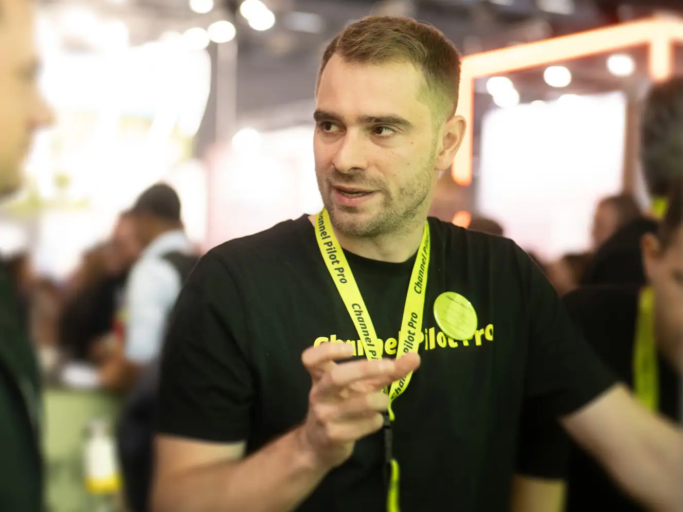 Der Mann spricht auf einer Messe oder Konferenz, trägt ein schwarzes T-Shirt mit Logo und eine gelbe.