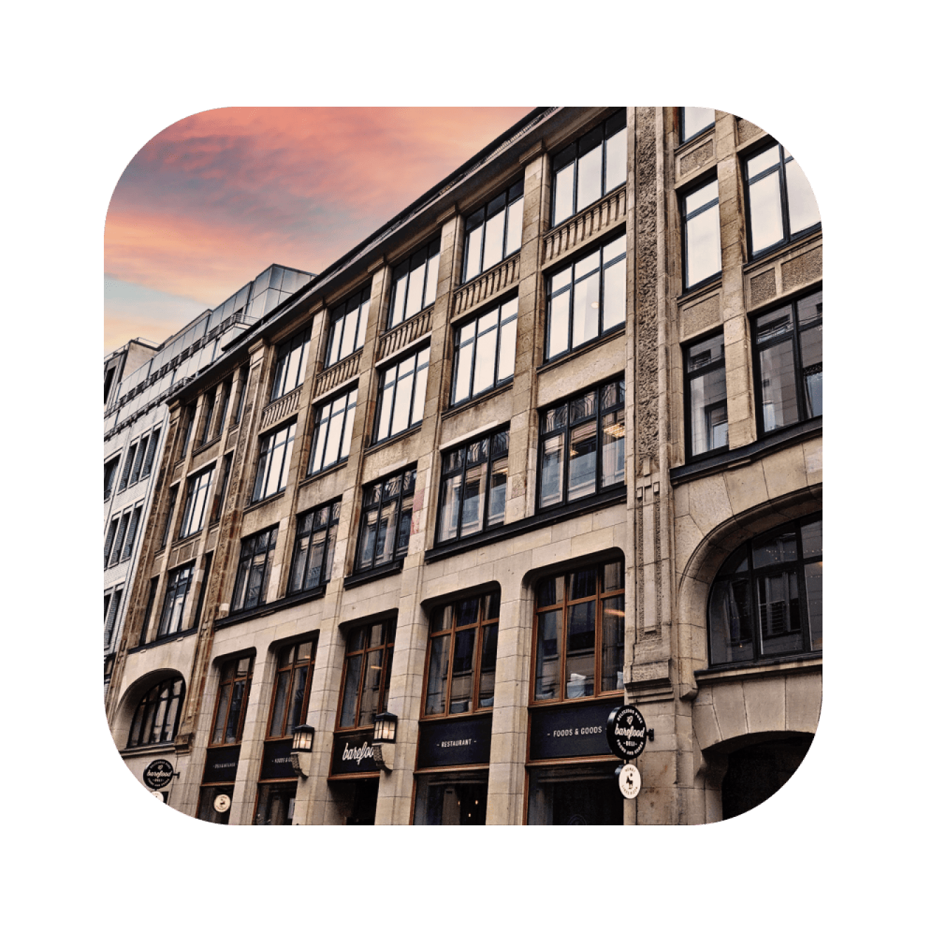 Altbau-Fassade mit großen Fenstern und Steinarchitektur bei Sonnenuntergang.