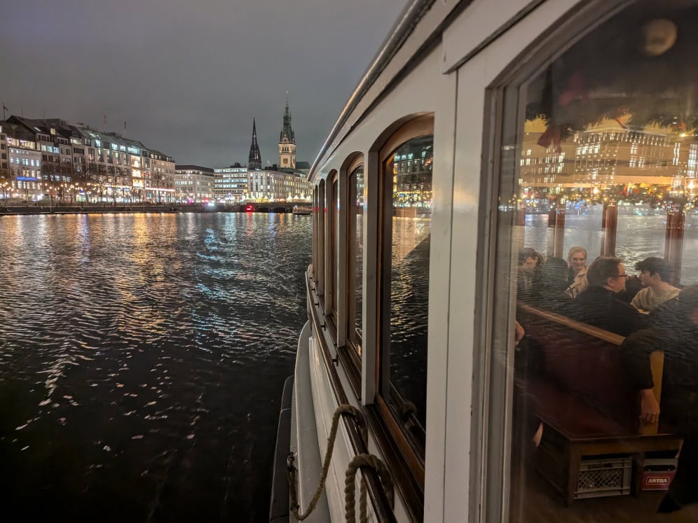 Ein Boot auf dem Fluss bei Nacht mit Blick auf die Stadt und beleuchtete Gebäude.